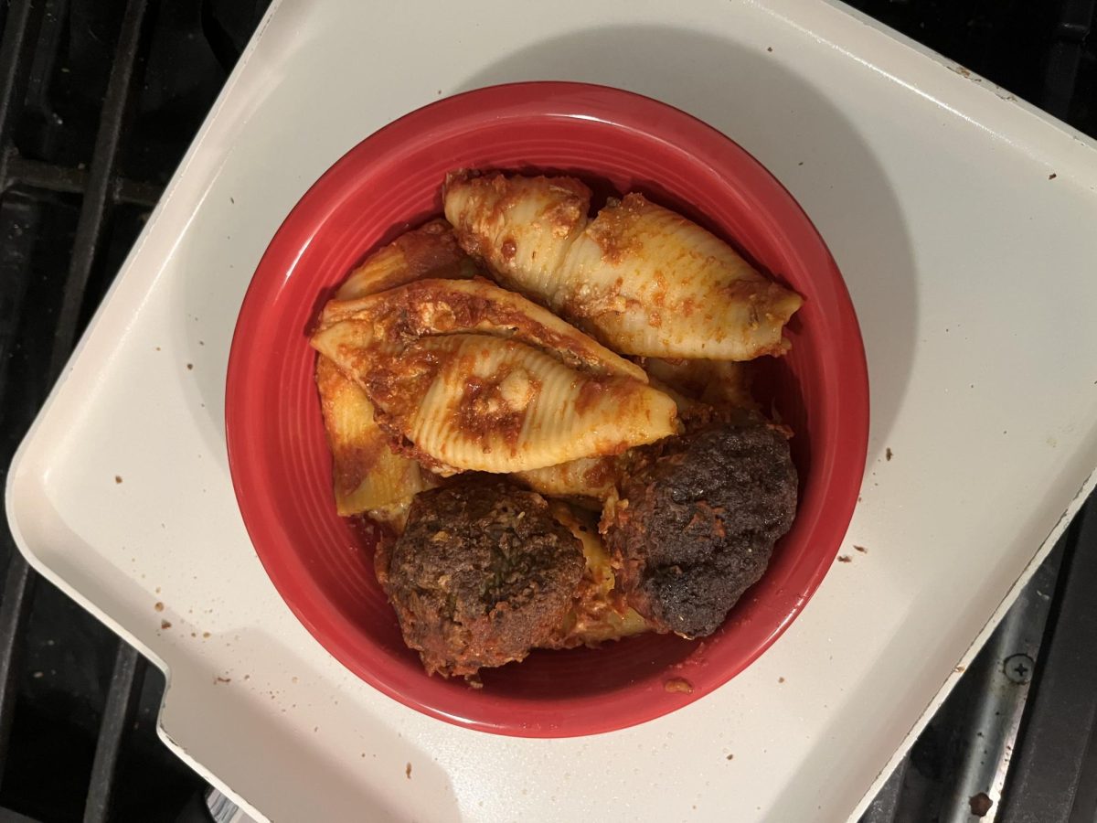 A bowl of leftover stuffed shell pasta and meatballs, covered in homemade tomato sauce, sitting on a stove.