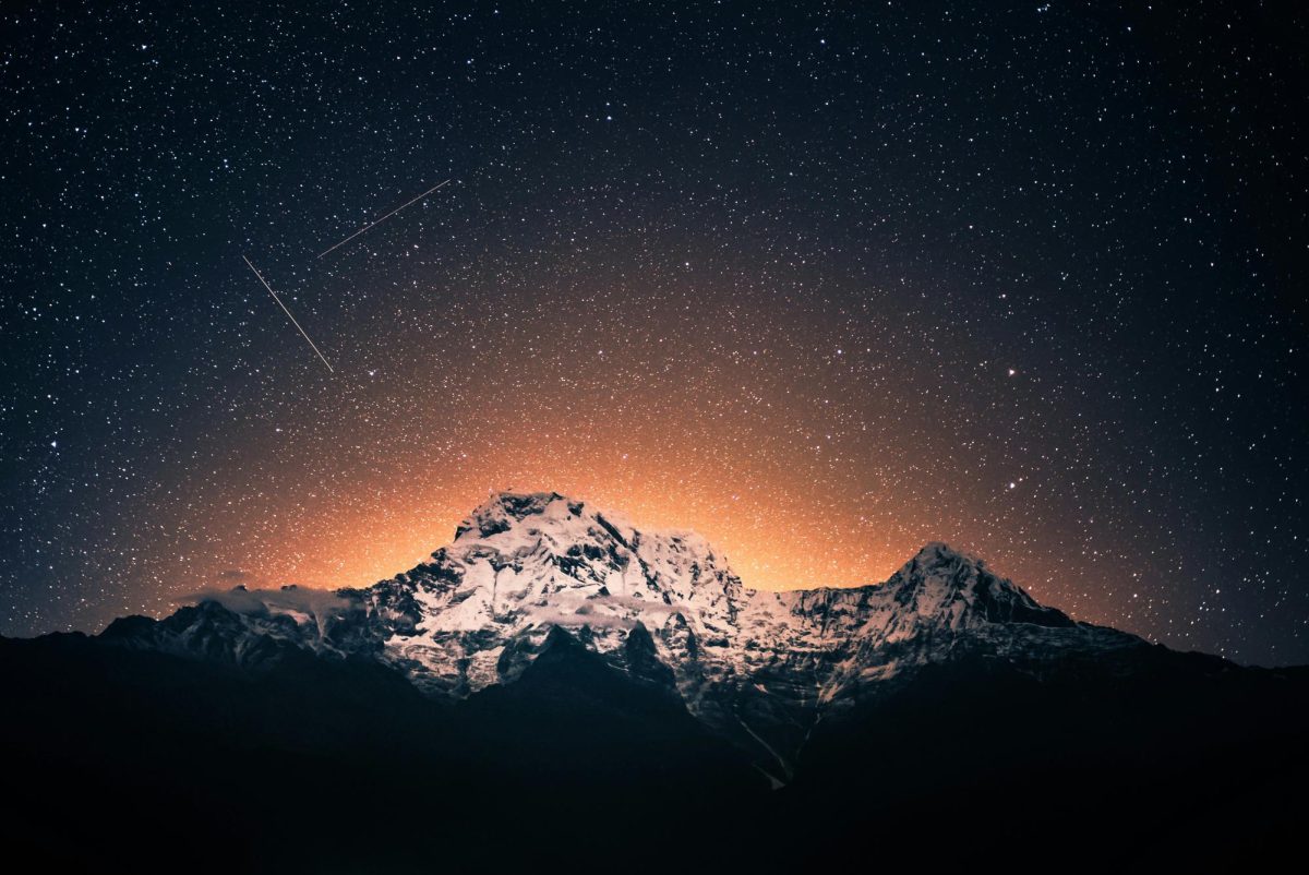 A meteor shower in a starry sky above a mountain range, with light emanating from behind it. Image courtesy of Unsplash